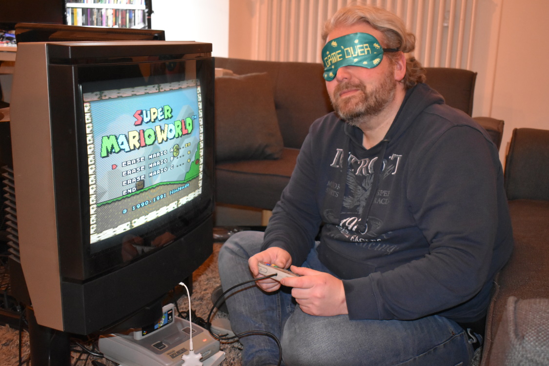 Ein Gamer sitzt mit verbundenen Augen vor einem Super Nintendo und spielt